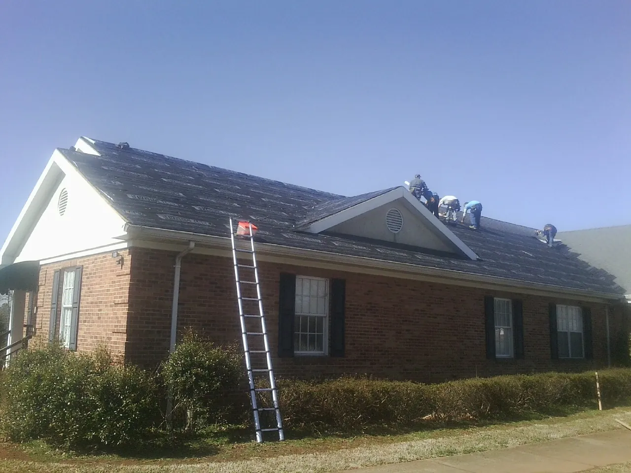 Crew tearing shingles off a brick ranch roof with a ladder set — Emergency Roof Repair work by our crew in Los Alamitos