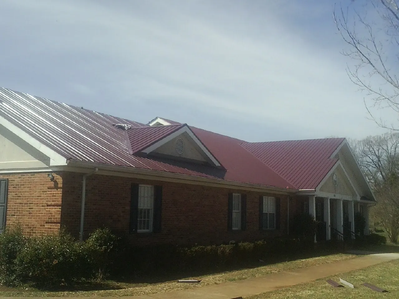 Red metal roof with gabled entries on a long brick building, from a Hail Damage Roof Repair job in Los Alamitos