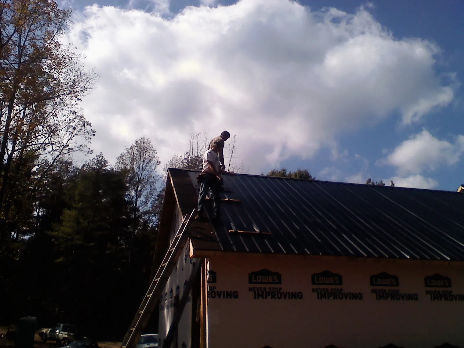 Roofer fastening dark metal panels high against a cloudy sky, from a Roof Inspection job in Los Alamitos