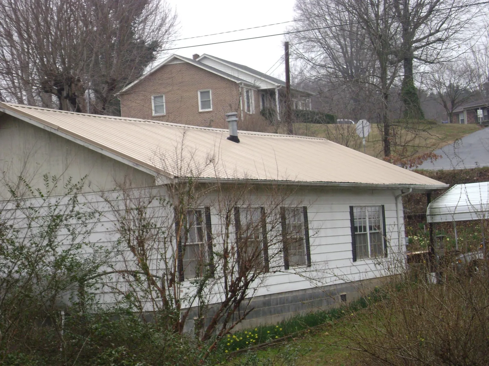 Tan metal roof on a white sided house set into a hillside — Commercial Roofing by Roofing Brothers in Los Alamitos